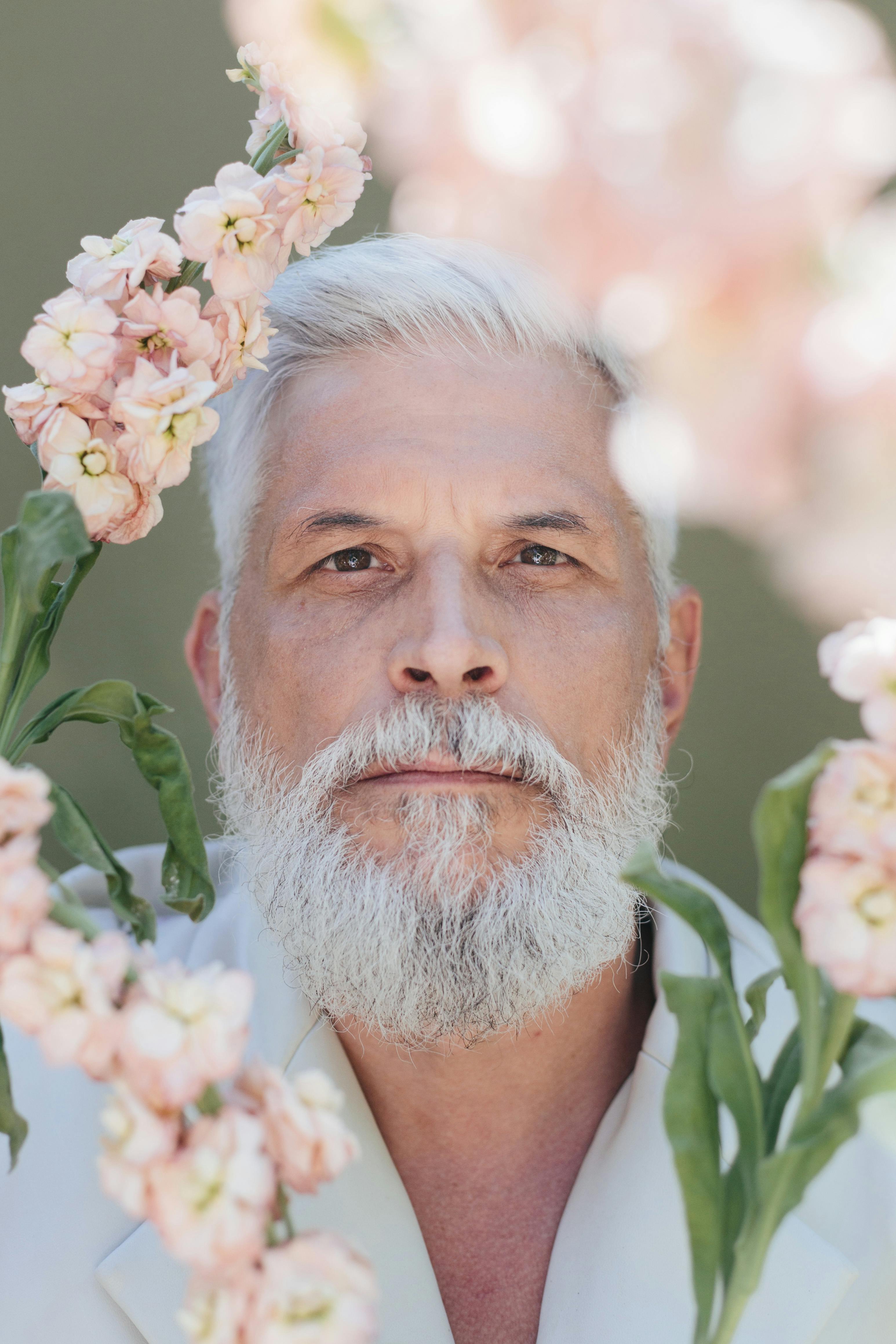 Rustic man with beard happy face enjoy life in ecological environment.  Hipster with lilac flowers looks happy. Bearded man with lilac in beard  green grass background. Eco friendly lifestyle concept Stock Photo 