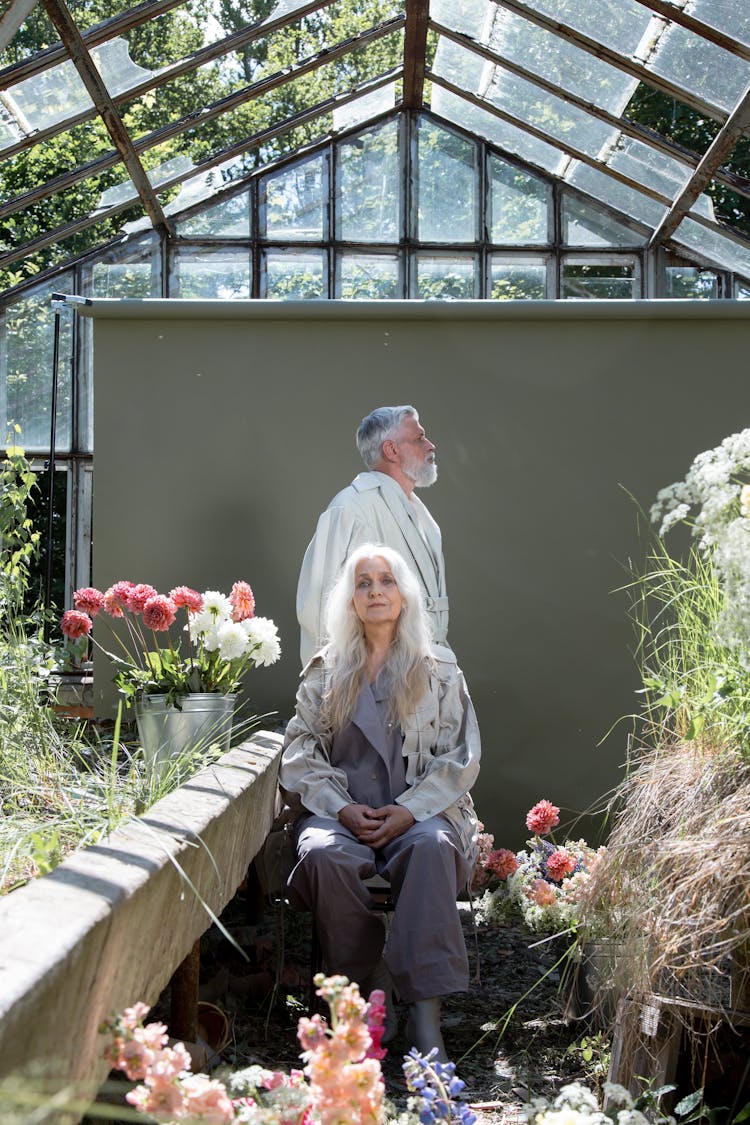 Elderly Man And Woman Sitting In A Greenhouse With Flowers