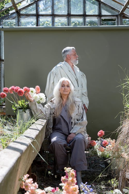 An Elderly Couple Wearing Long Sleeve Coats Near Pots of Flowers