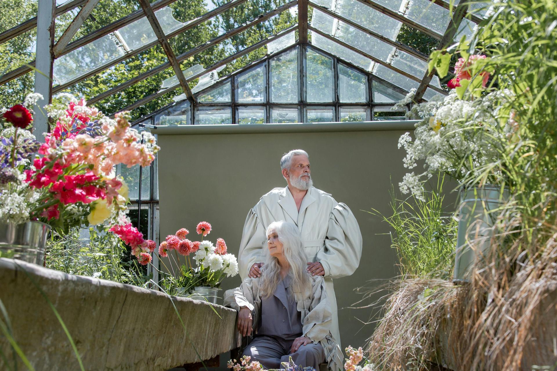 An Elderly Couple Sitting and Standing in a Damaged Greenhouse