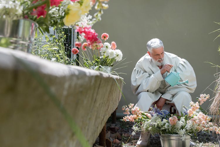 An Elderly Man Watering Flowers In A Bucket