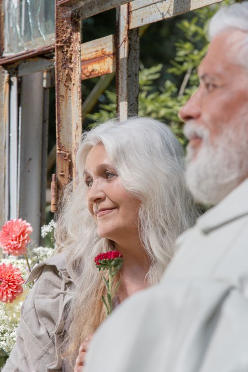 Free Charming elderly couple enjoys a serene garden moment, holding vibrant flowers. Stock Photo