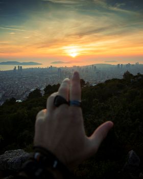 A hand pointing toward a vibrant sunset over a sprawling urban landscape in Turkey.