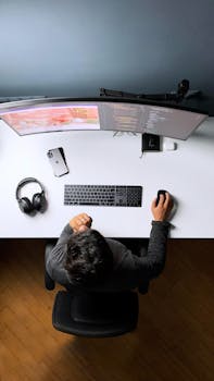 Top view of a person working at a computer desk with dual monitors, headphones, and smartphone.