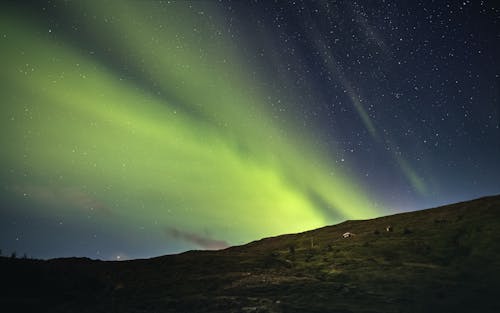 A Green Aurora Borealis on Night Sky Over a Hill