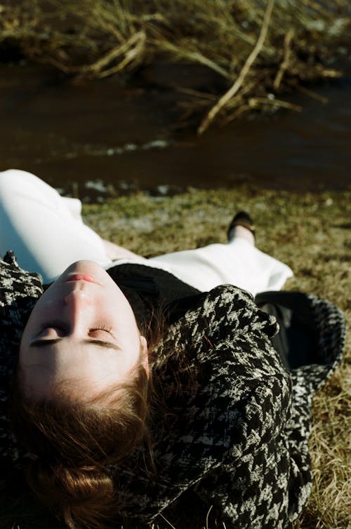 Free A Young Woman in Black and White Coat Lying on Grass Stock Photo