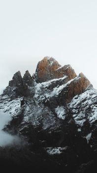 Stunning vertical shot of a snow-capped rocky mountain peak against a white sky. 10051137