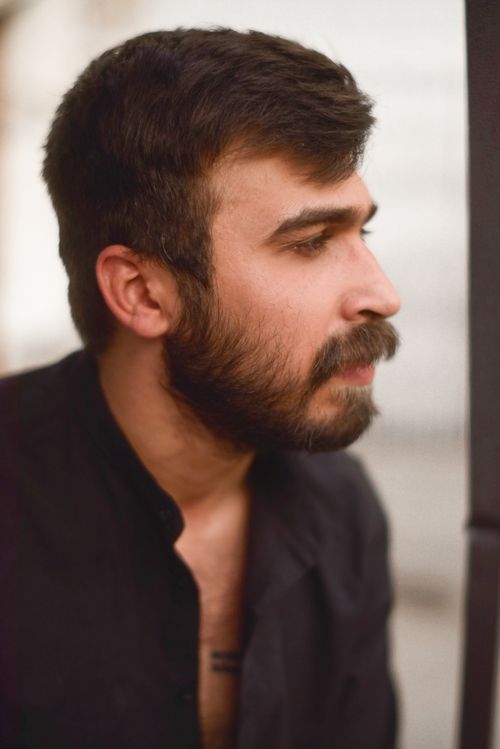 Free Close-up side profile of a bearded man in a black top, looking thoughtful. Stock Photo