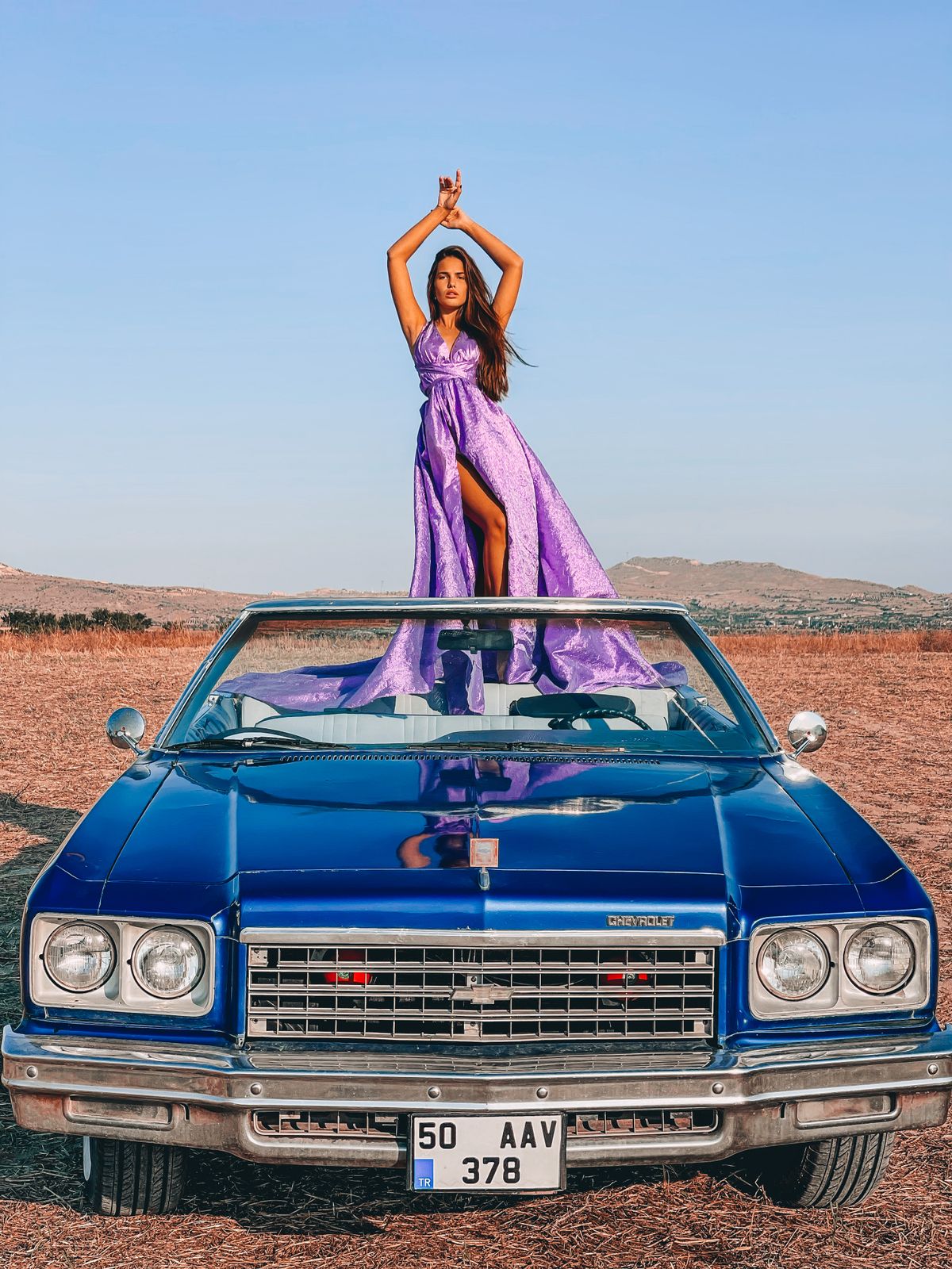 A woman in a purple dress standing on a vintage blue convertible — the loud luxury lifestyle