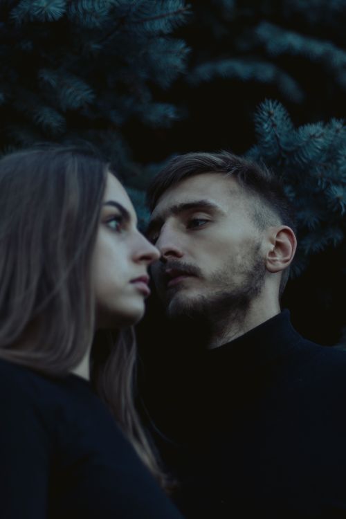 Free A couple standing close together in an outdoor setting, gazing intently. Moody and dark atmosphere. Stock Photo
