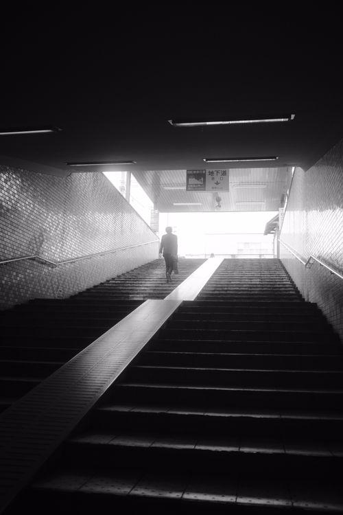 Free Dramatic black and white photo of a person walking up subway stairs, capturing solitude. Stock Photo