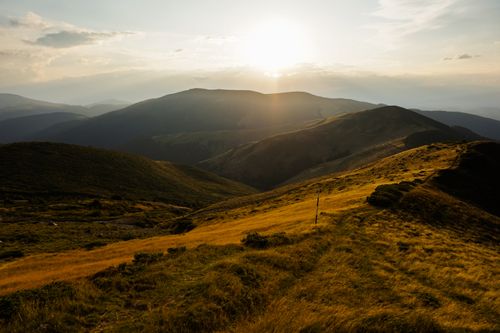 Free Beautiful golden sunset over lush green hills and valleys, creating a serene landscape. Stock Photo