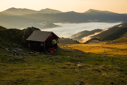 这是一座坐落在薄雾笼罩的乡村景观中的孤独小屋，拥有优美的山景，尤其在日落时分