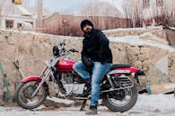 在白雪皑皑的印度户外，一名男子坐在红色摩托车上