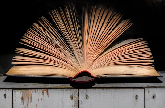 An open vintage book displayed on a wooden surface with dramatic lighting emphasizing its textured pages.