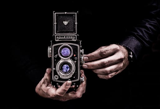 Close-up of hands holding a classic vintage Rolleicord camera against a dark background.