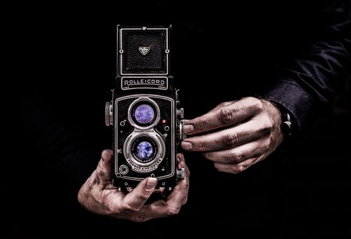 Free Close-up of hands holding a classic vintage Rolleicord camera against a dark background. Stock Photo