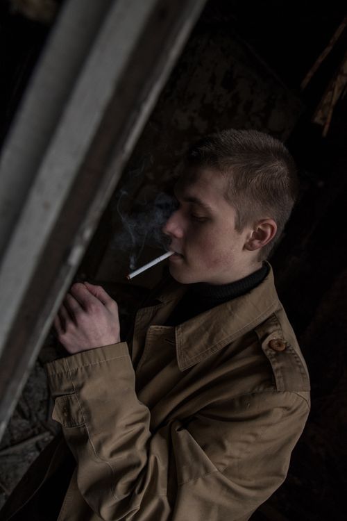 Free A man in a trench coat smoking a cigarette in a dimly lit outdoor setting, evoking a mysterious and moody vibe. Stock Photo
