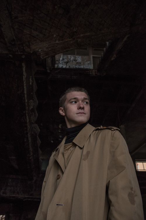 Free Moody portrait of a man in a trench coat looking away in an abandoned urban setting. Stock Photo