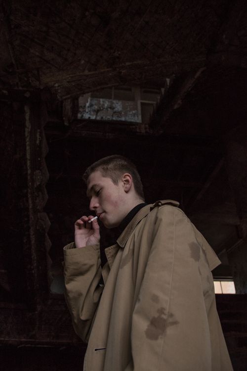 Free A contemplative man in a coat smokes in a dim urban environment, showcasing solitude. Stock Photo