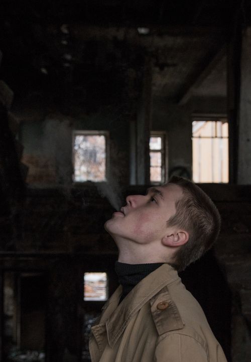Free Side view of a man exhaling smoke in a dimly lit, abandoned building. Stock Photo