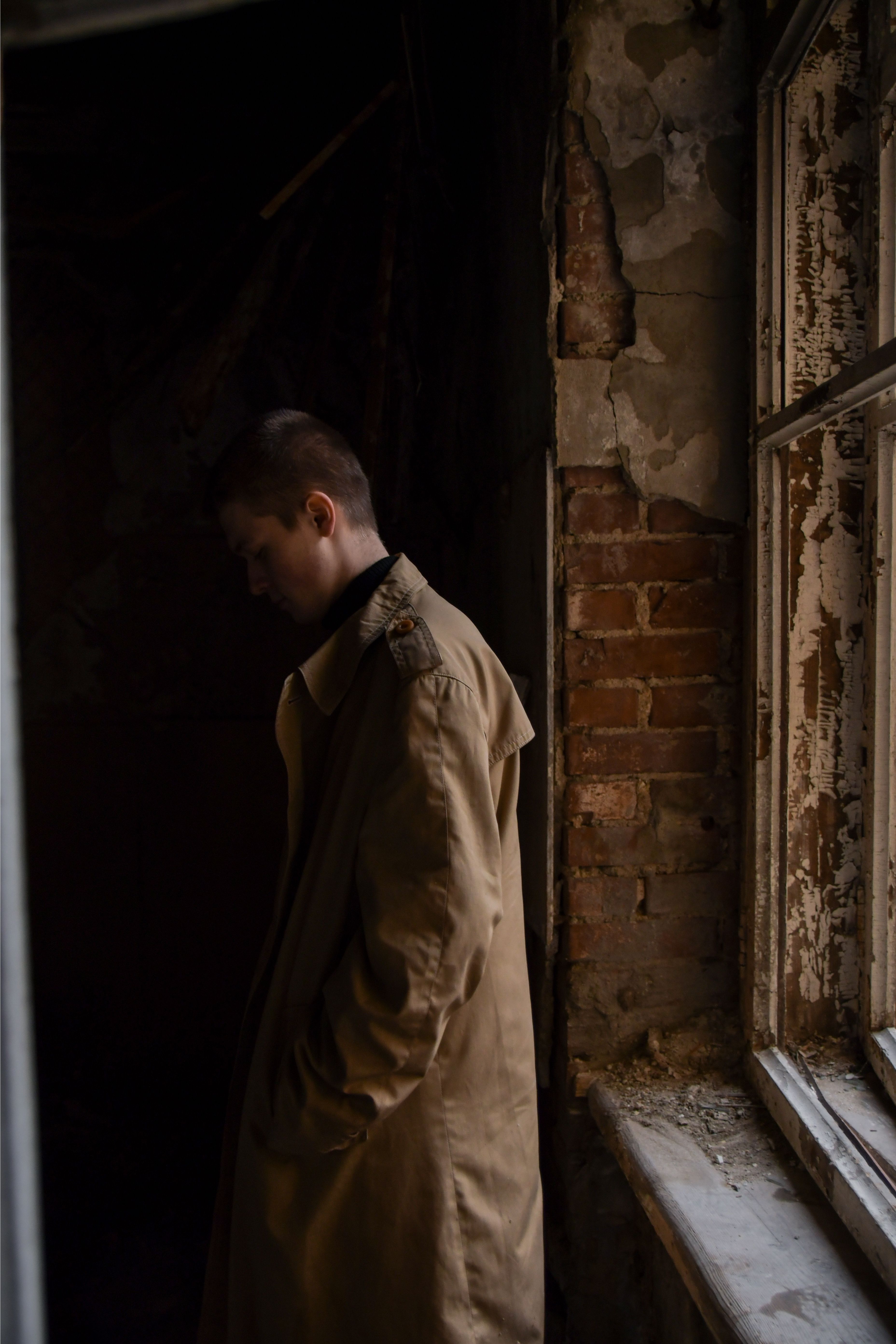Silhouette of a man in a beige coat standing in an abandoned building next to a window.