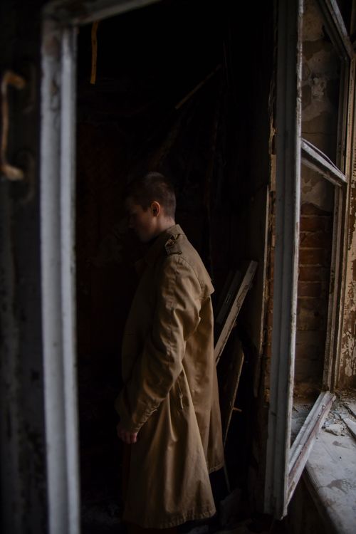 Free A man in a brown coat stands in an eerie, abandoned room with damaged walls. Stock Photo