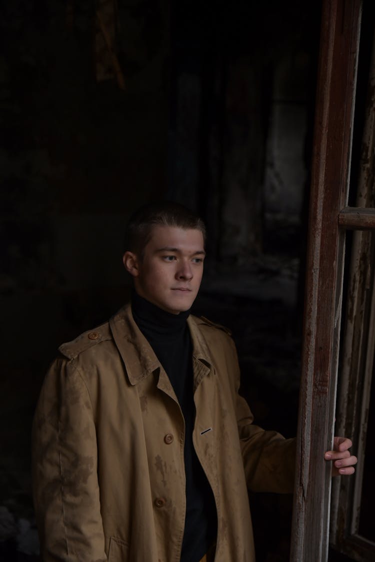 A Boy In Brown Coat Holding On A Wooden Door Frame