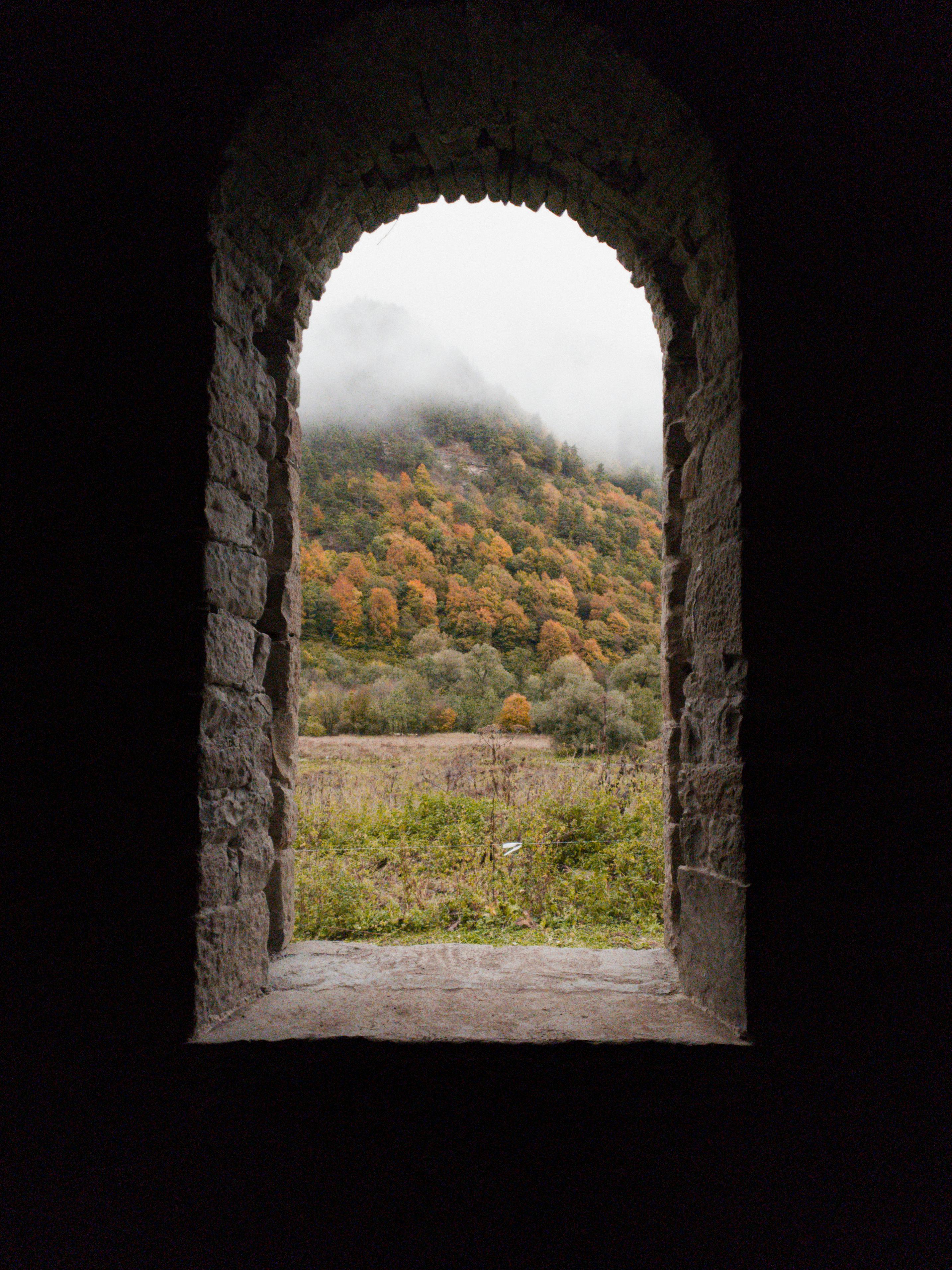 Looking through a stone arch window at a foggy, colorful autumn forest in Arkhyz, Russia.