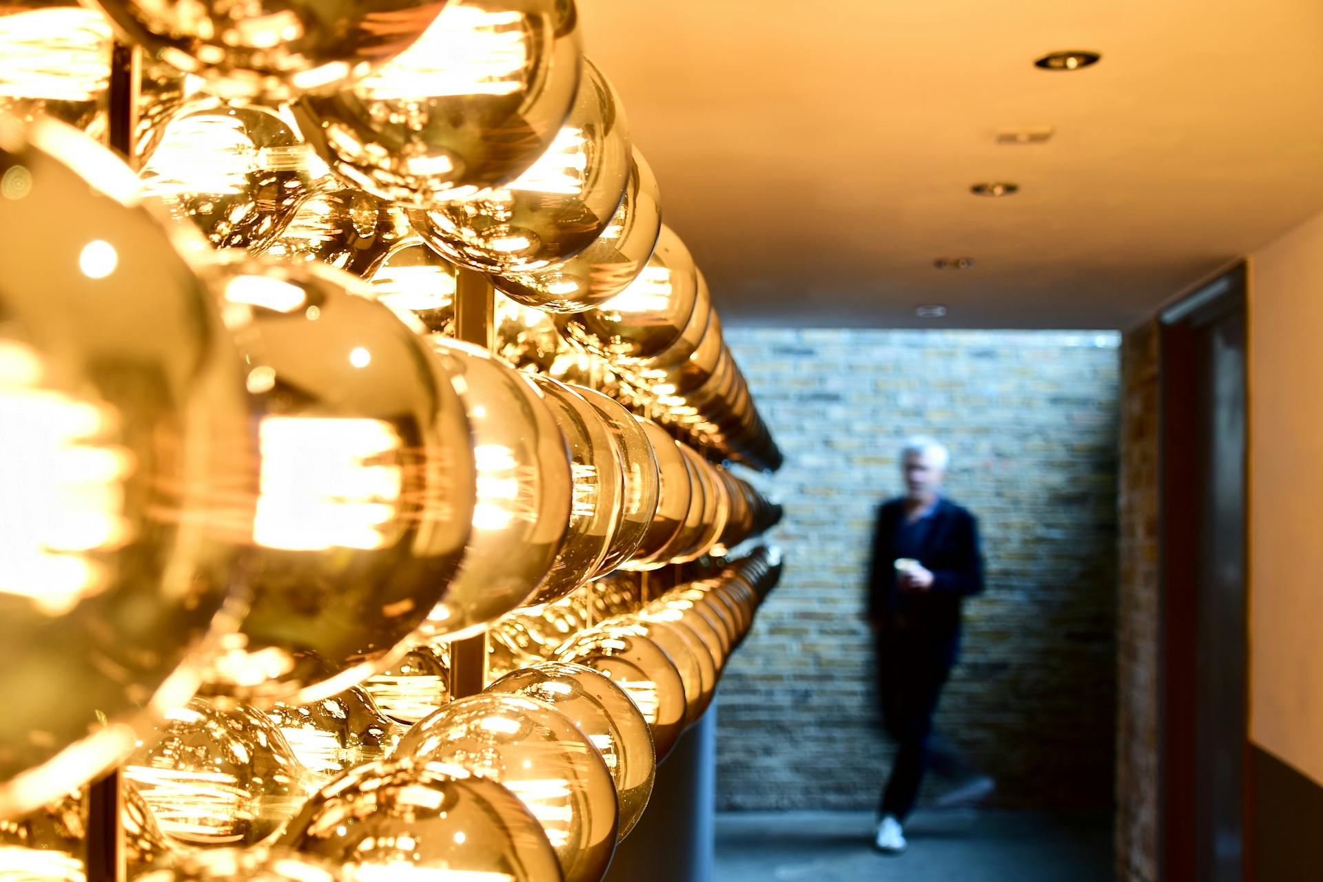 Blurred man in modern hallway with gold spherical lights. Indoor architectural detail.