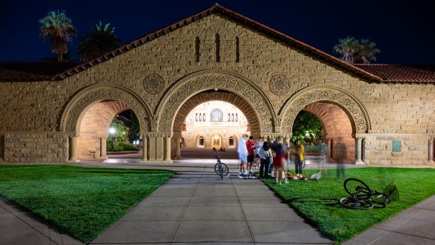 Nighttime view of Stanford University's iconic arch with a group of people and bikes.