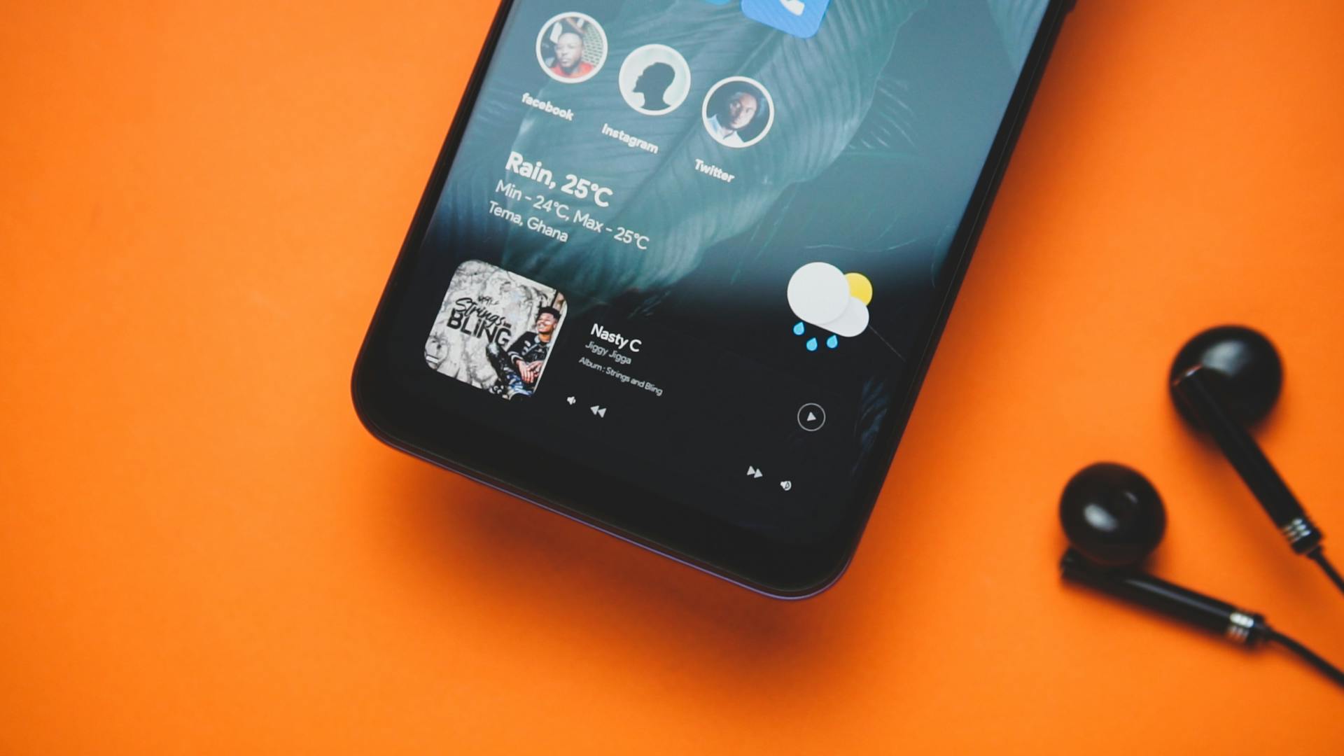 Close-up of a smartphone with earphones on an orange background showing a music playlist and weather update.