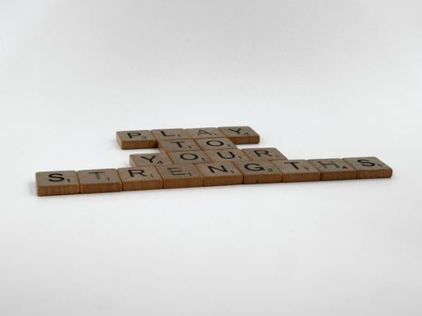 Wooden Scrabble tiles arranged to spell 'Play to your strengths' on a white surface.