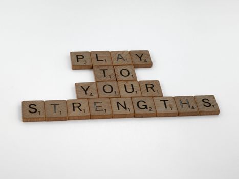 Motivational message 'Play to Your Strengths' made from wooden Scrabble tiles on a white background.