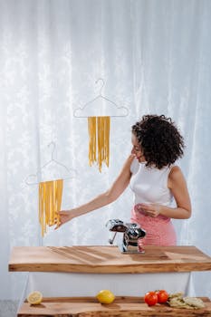 Woman with curly hair hangs fresh pasta using hangers in a modern kitchen.