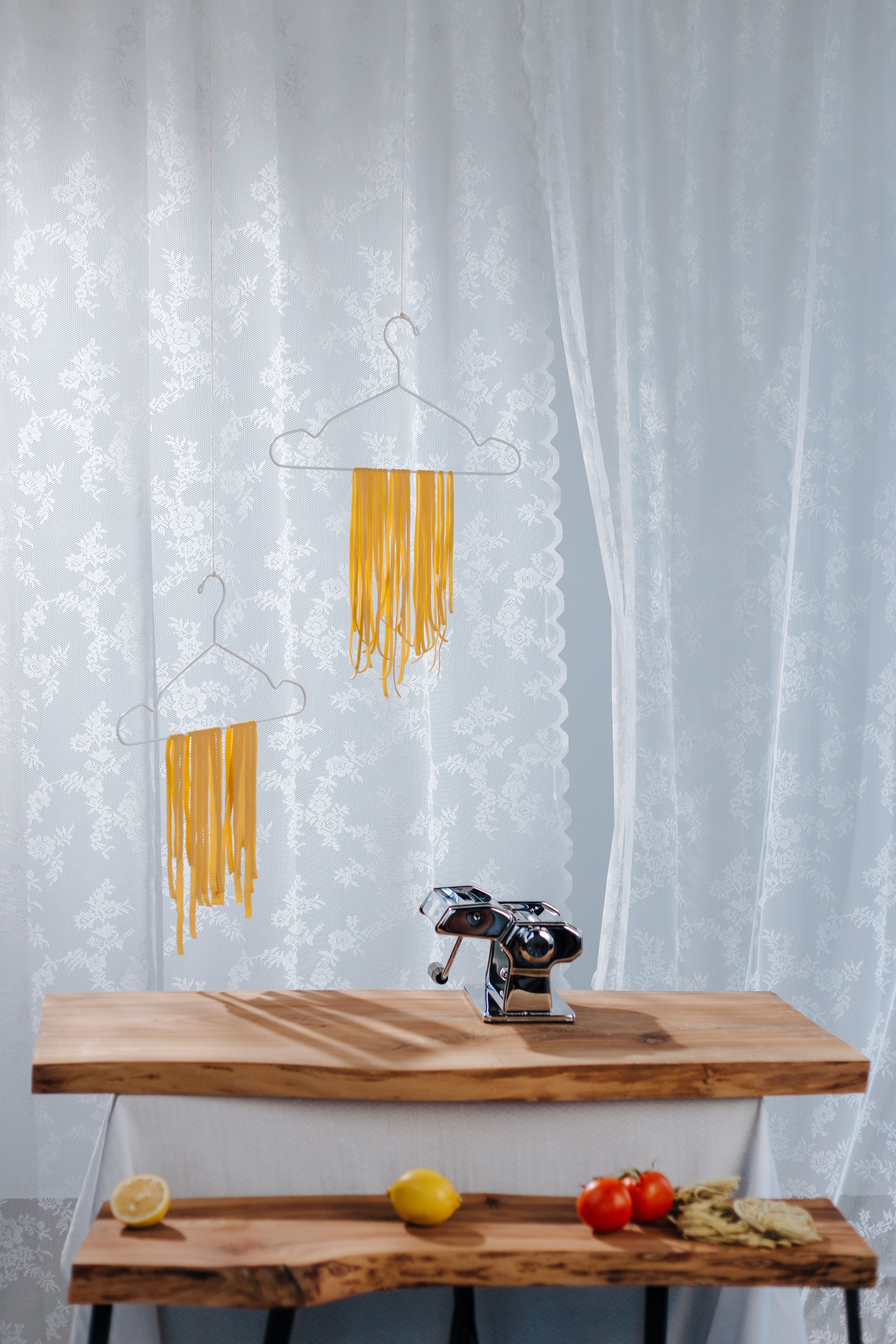 Artistic kitchen scene with pasta drying creatively on hangers with fresh ingredients.