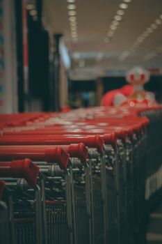 Red shopping carts lined up in a supermarket aisle, depth of field highlights cart details.