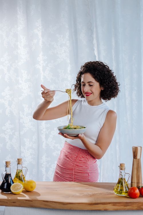Free Young woman with curly black hair enjoying a bowl of Italian pasta indoors. Stock Photo
