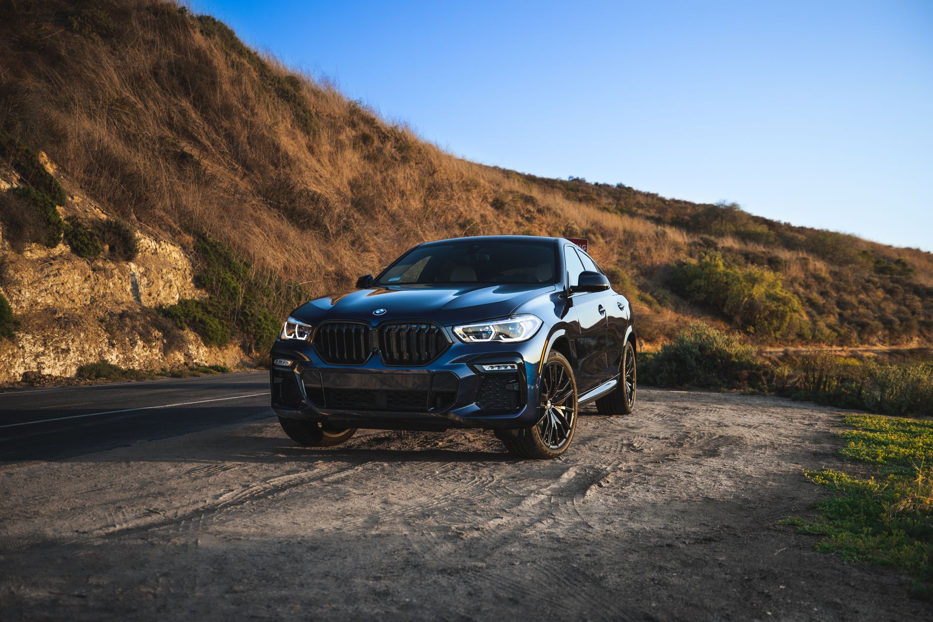 Blue BMW X6 M parked on a scenic road in Newport Beach, CA at sunset.