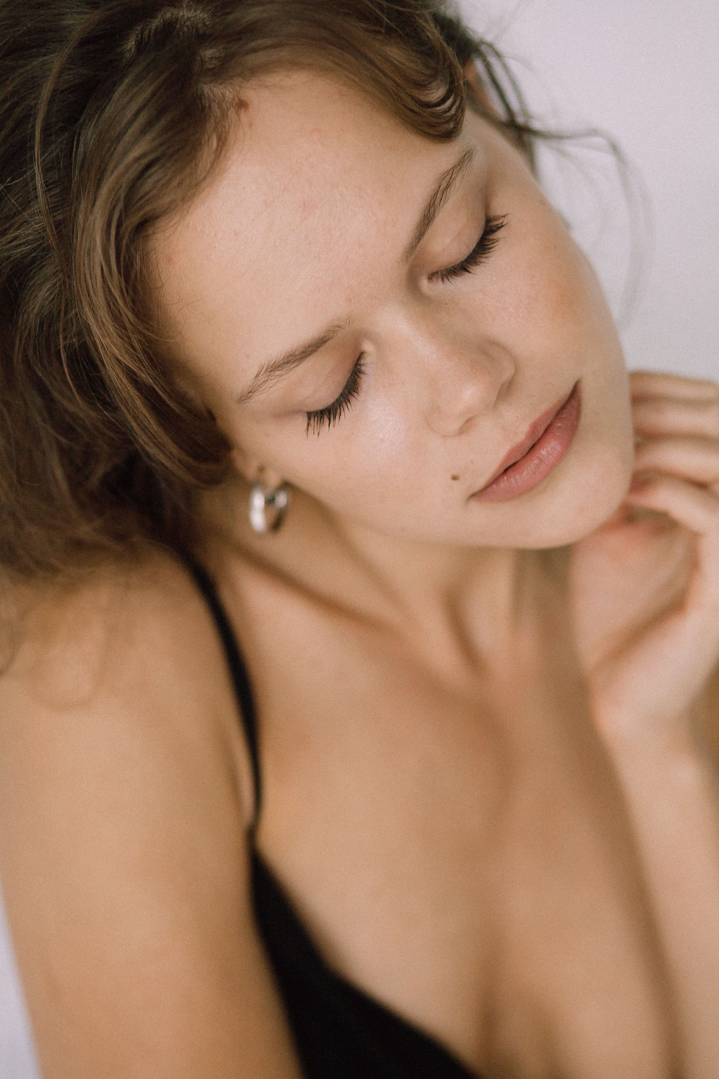 Relaxed young woman with eyes closed in a soft, serene pose, wearing a black top.