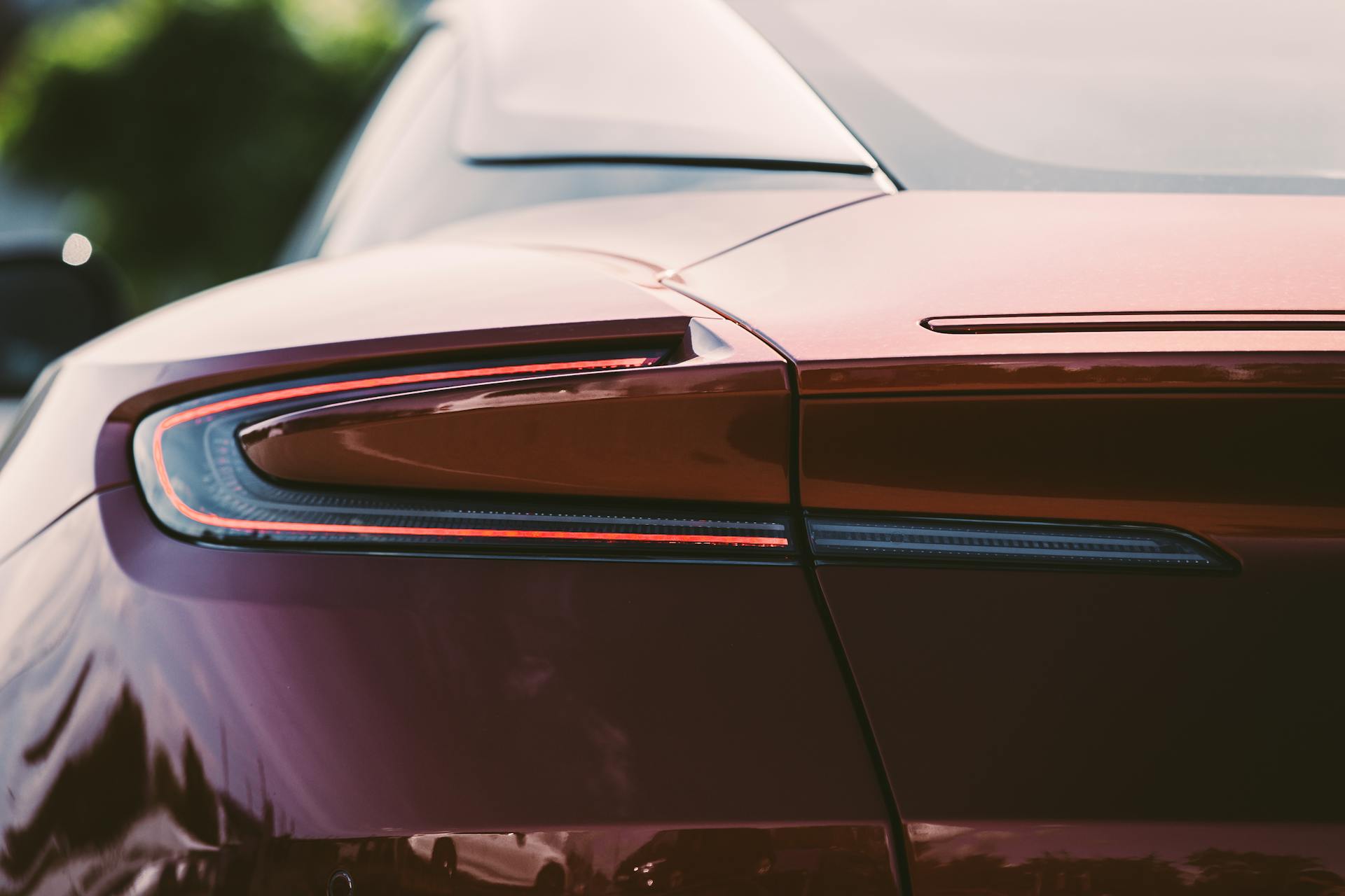 Detailed shot of a modern red luxury sports car's rear design with sunlight reflections.