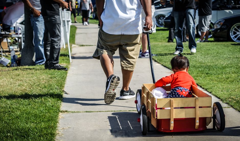 A man pulls a child in a red wagon during an outdoor event on a sunny day.