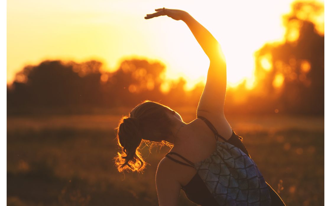 A woman performs a stretching exercise outdoors at sunrise, embracing fitness during the serene golden hour.