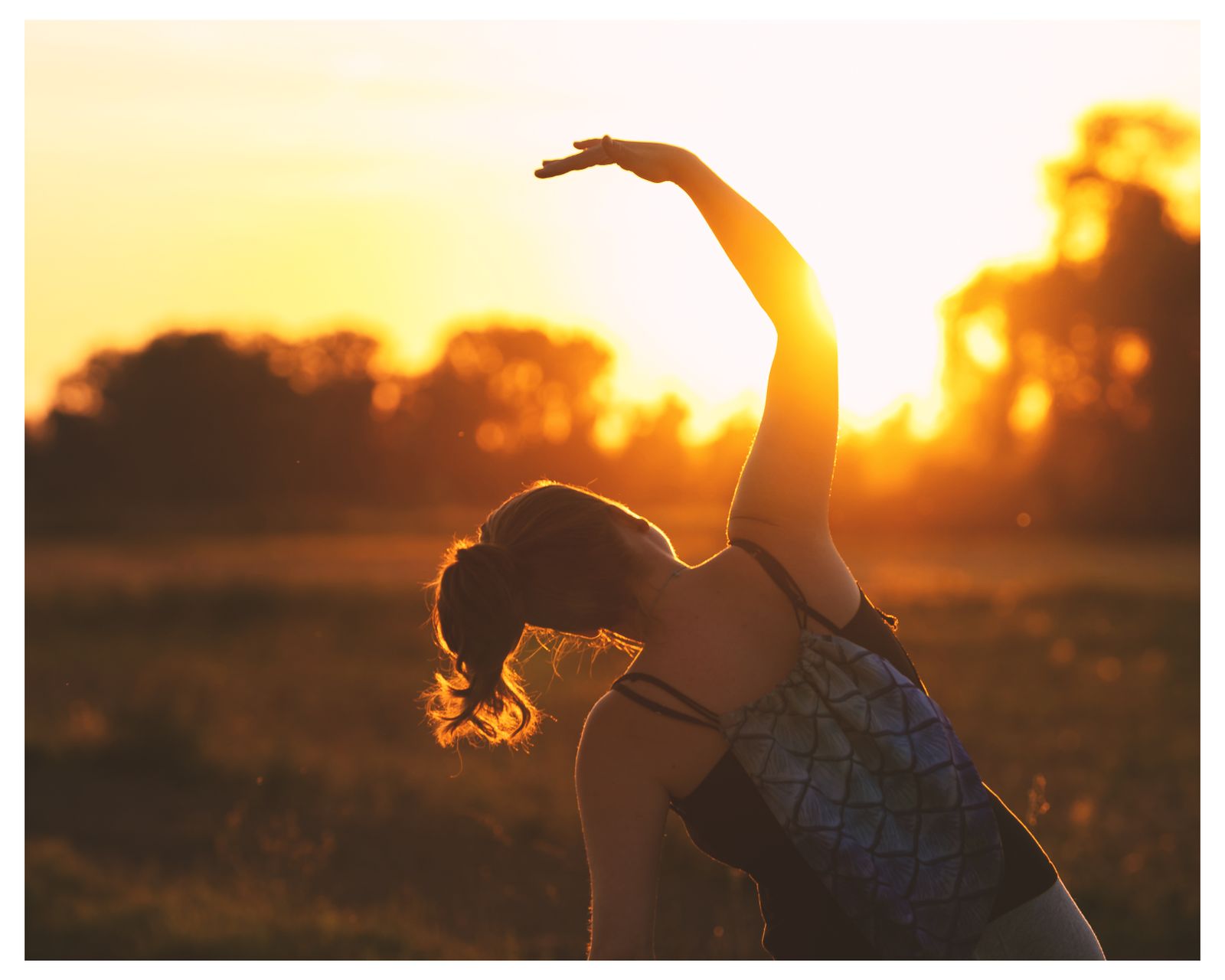 Silhouette of a woman in a backbend yoga stretch at golden hour in an open field
