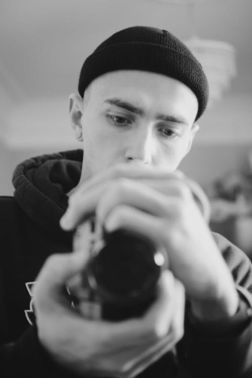 A Grayscale Photo of a Man in Knitted Cap Holding a Camera