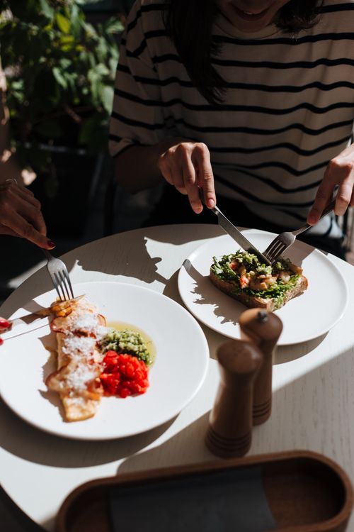 Free A relaxed dining scene with individuals slicing fresh meals at a round table. Stock Photo