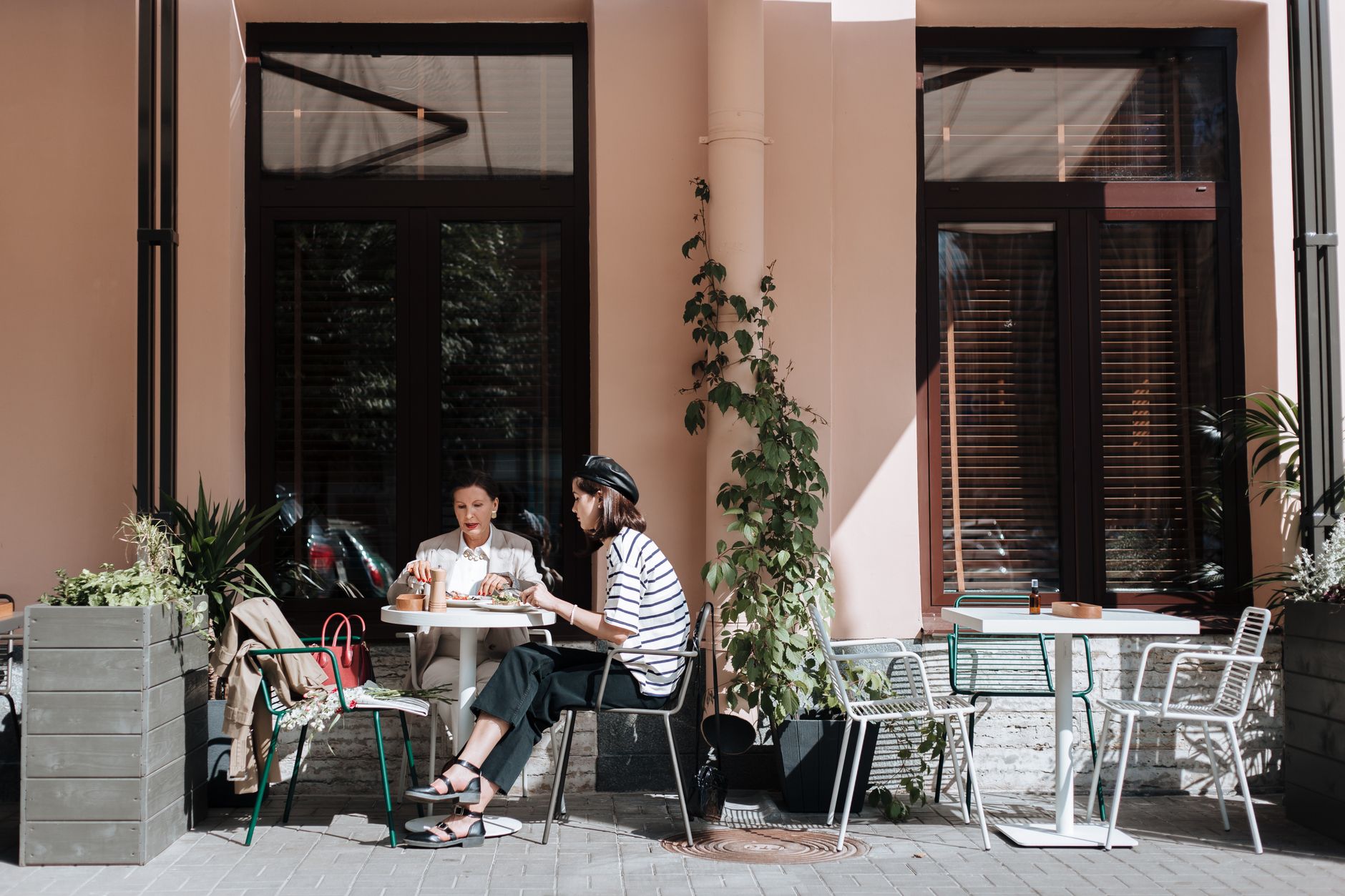 Two women talking over lunch at an outdoor cafe, one leaning forward as if the small detail matters