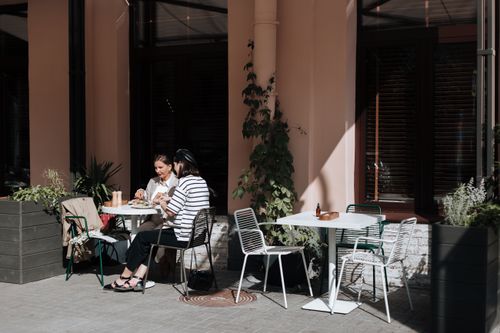 Free Two women enjoy an outdoor brunch at a charming cafe surrounded by plants. Stock Photo