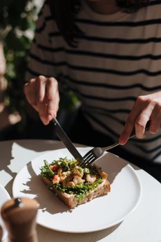 Person slicing an open-faced vegetable sandwich on a white table in a cozy café.