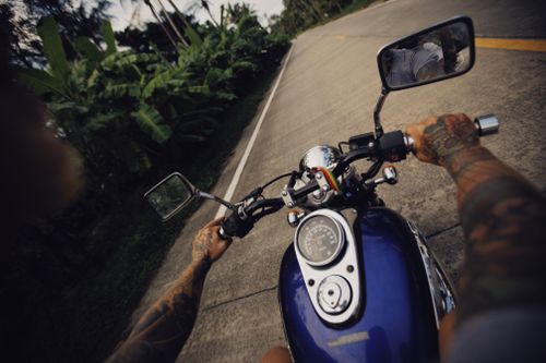 Free Tattooed motorcyclist rides along a scenic road, showcasing freedom and adventure. Stock Photo